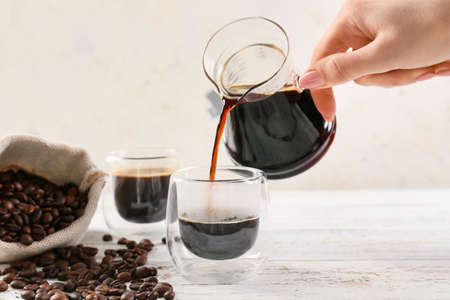 Woman pouring turkish coffee from pot into cup on light wooden background