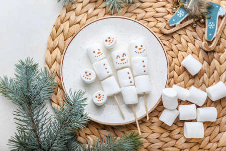 Plate with snowmen made of soft marshmallows on white background