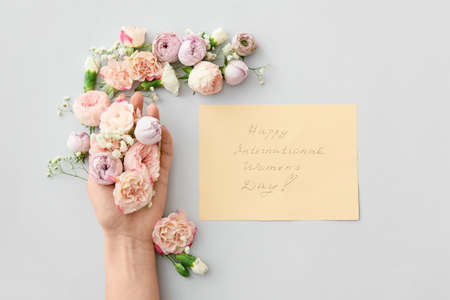 Hand with beautiful flowers and card for International Women's Day on light backgroundの写真素材