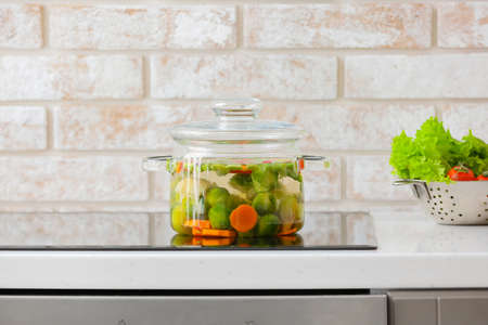 Stylish cooking pot with vegetables on stove in kitchen