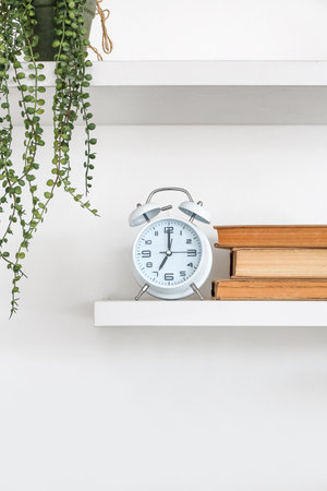 Book shelves with alarm clock hanging on light wallの写真素材