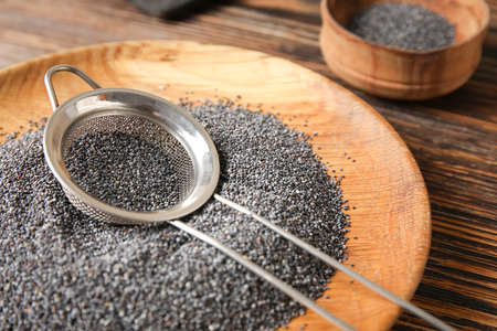 Plate and sieve with poppy seeds on wooden backgroundの写真素材