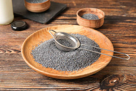 Plate and sieve with poppy seeds on wooden backgroundの写真素材