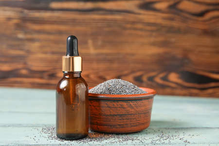 Bowl with poppy seeds and bottle of oil on color wooden backgroundの写真素材