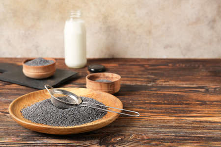 Plate and sieve with poppy seeds on wooden backgroundの写真素材