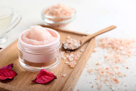 Board with jar of body scrub, sea salt and flower petals on light backgroundの写真素材