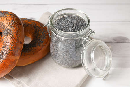 Jar with poppy seeds and tasty bagels on light wooden backgroundの写真素材