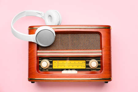 Retro radio receiver with headphones on color background