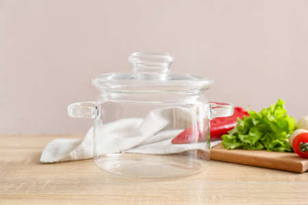Stylish cooking pot and vegetables on light wooden background