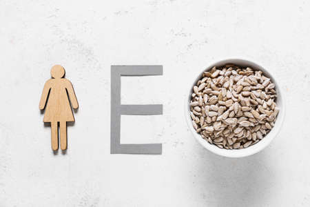 Bowl with sunflower seeds, female figure and letter E on grunge background