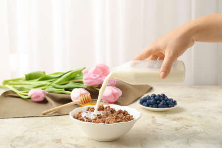 Woman pouring milk from bottle into plate with granola on tableの写真素材