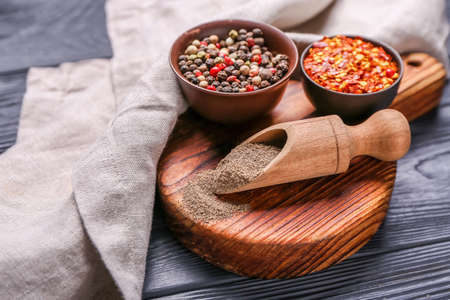 Board with different types of pepper on dark wooden background