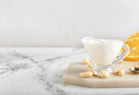 Gravy boat with cashew sour cream, nuts and lemon on light backgroundの写真素材