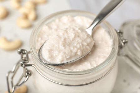Jar and spoon with cashew sour cream on light background, closeupの写真素材