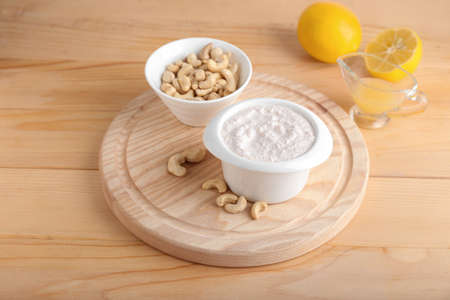 Bowls with cashew sour cream, nuts and lemon juice on wooden backgroundの写真素材