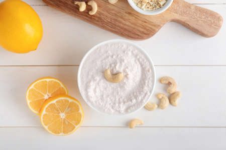 Bowl with cashew sour cream, nuts and lemon on light wooden backgroundの写真素材