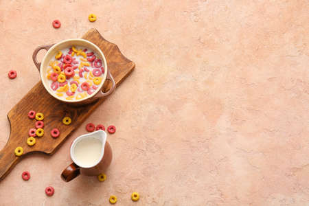 Bowl with colorful cereal rings and jug of milk on color backgroundの写真素材