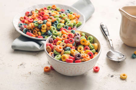Bowl and plate of colorful cereal rings on light grunge background