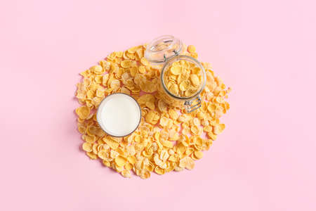 Glass of milk and jar with tasty cornflakes on color backgroundの写真素材