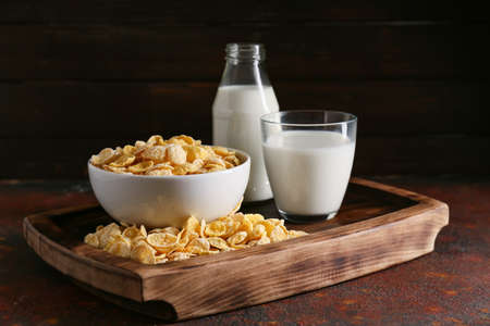 Glass of milk and bowl with tasty cornflakes on grunge backgroundの写真素材