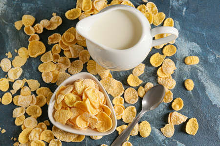 Bowl with tasty cornflakes and jug with milk on color background