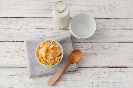 Bowl with tasty cornflakes and bottle of milk on light wooden backgroundの写真素材
