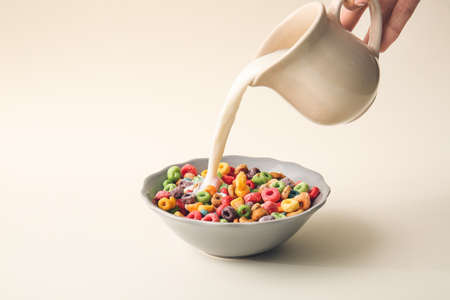 Pouring milk in bowl of colorful cereal rings on light backgroundの写真素材