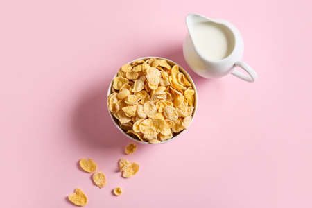 Bowl with tasty cornflakes and jug of milk on color backgroundの写真素材