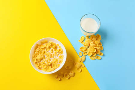 Bowl with tasty cornflakes and glass of milk on color backgroundの写真素材