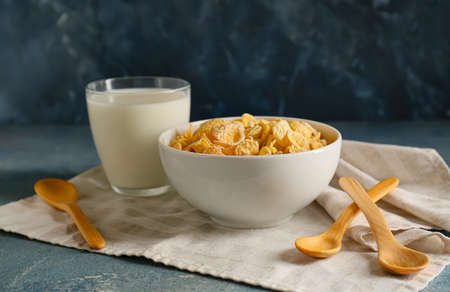 Bowl with tasty cornflakes and glass of milk on color background