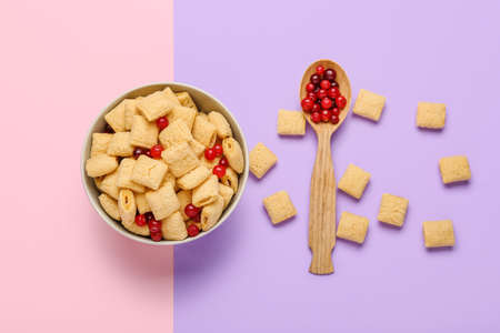 Bowl with tasty corn pillows and cranberries on color background