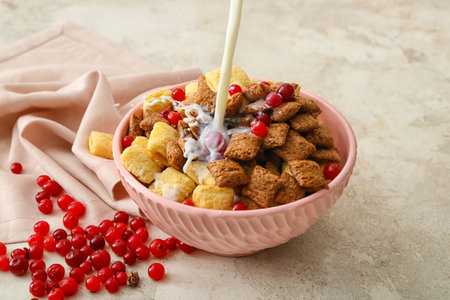 Pouring of milk into bowl with tasty corn pillows and cranberries on light background
