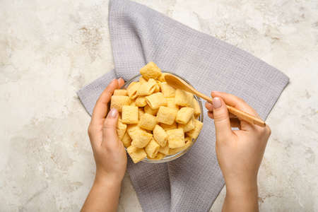 Woman eating tasty corn pillows on light background