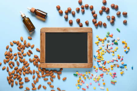 Empty chalkboard with healthy nuts, pills and oil on color backgroundの写真素材