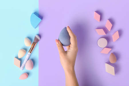 Female hand with stylish makeup sponges and brush on color backgroundの写真素材