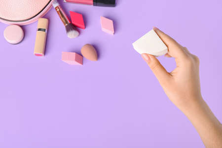 Female hand with stylish makeup sponge and decorative cosmetics on color backgroundの写真素材