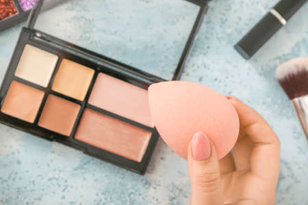Female hand with stylish makeup sponge and decorative cosmetics on color backgroundの写真素材