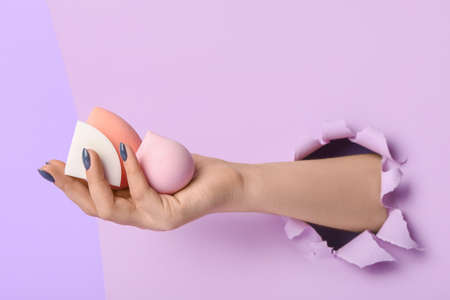 Female hand with stylish makeup sponges on color backgroundの写真素材