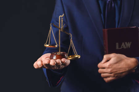 Male lawyer with book and scales of justice on dark backgroundの写真素材