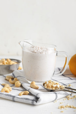 Jug of sour cream with cashew nuts on light backgroundの写真素材
