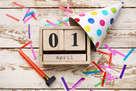 Party decor and calendar with date of April Fools Day on white wooden background