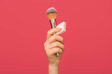 Female hand with stylish makeup sponge and brush on color backgroundの写真素材