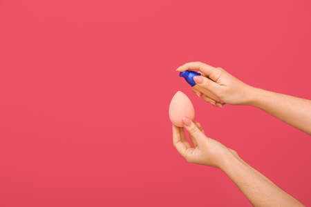 Woman putting foundation on makeup sponge on color backgroundの写真素材