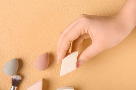 Female hand with stylish makeup sponge and decorative cosmetics on color backgroundの写真素材
