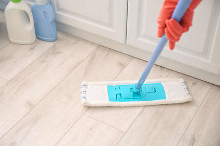 Young man mopping floor in kitchen, closeup