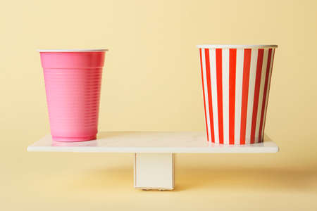 Plastic and paper cups on teeterboard against color background. Concept of balanceの写真素材