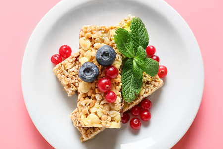 Plate with healthy cereal bars and berries on color background