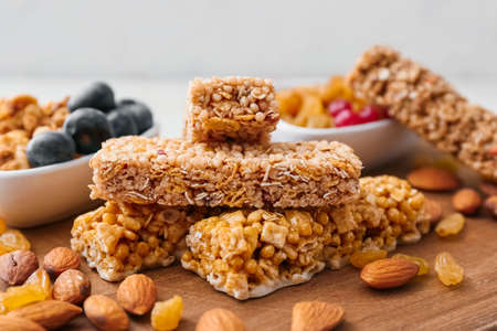 Board with healthy cereal bars, berries and nuts on light background