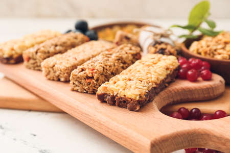Board with healthy cereal bars and berries on light backgroundの写真素材