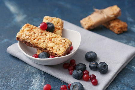 Bowl with healthy cereal bars and berries on color background